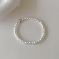 Bracelet élégant en perles blanches avec un zircon central sur un fond beige texturé - Bracelet de perles blanches