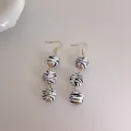 Détail de longues perles en bois zébrées avec des capsules dorées et des crochets d'oreille - Zèbre Noir et Blanc