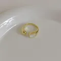 Close-up of minimalist gold shell ring with polished metal sphere and white inlay - Gold