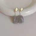 Dettaglio di orecchini lunghi in resina con trama in marmo grigio e cornice dorata - Grigio