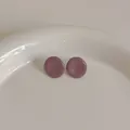 Detail von runden mauve Emaille-Ohrsteckern auf einem weißen Porzellanteller im minimalistischen Stil - Lila