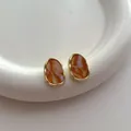 Detailansicht unregelmäßiger Goldohrringe mit orangefarbenem Marmorharz-Inlay auf Tablett - Gelbe Tarnung