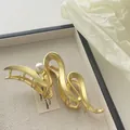 Detailed macro view of matte gold metal hair clip with pearl on a textured tray - Pearl Wave Style (R10)