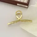 Detailopname van de matgouden haarklem met elegant gedraaid ontwerp op houten dienblad - Mat Goud