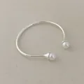 Detailed close-up of a silver metal open bangle with white pearls on a linen fabric - Pearl Bangle
