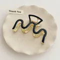 Macro shot of M-shaped golden metal hair claw with black enamel wave detail on tray - Black I-192