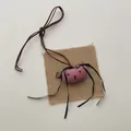 Handgemaakte roze stoffen beer hanger met bruine draagriem op een linnen achtergrond - Roze