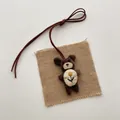 Detail eines braunen Cord-Plüschbären-Anhängers mit Stickerei und langer Kordel am Band - Bär mit Weißem Bauch und Blume
