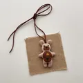 Close-up of a pink fabric cartoon bear plush pendant with embroidered floral detail - Brown Belly Flower Bear