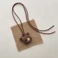 Close-up of handmade brown fabric bear pendant with detailed embroidery and rustic string - Brown Bear with Hat