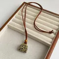 Detail van een gevlekte natuurstenen hanger met leren koord en houten kralenversiering - Dalmatijnse jaspis
