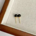 Detaillierte Nahaufnahme eleganter schwarzer Achat-Ohrstecker mit Vergoldung auf Stoff - Schwarz (6mm)