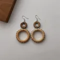 Close-up of bohemian rattan woven earrings with dark wood rings on white fabric - Coconut Shell Rattan Large Round (B349)