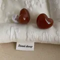 Detail of reddish-brown heart stud earrings with pearl backings on soft quilted fabric - Heart / Amber