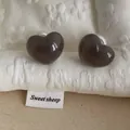 Detailed view of dark heart stud earrings with large white pearl backings on fabric - Heart / Gray