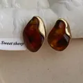 Dettaglio di orecchini in resina ambrata con bordo in metallo dorato e forma fluida moderna - Ambra