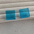 Detail of square blue acrylic stud earrings on a beige linen jewelry display tray - Blue