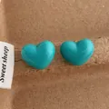 Close-up of bright turquoise heart-shaped stud earrings on a brown paper background - Heart / Blue