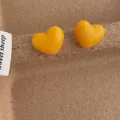 Detailaufnahme der hellgelben 3D-Herz-Ohrstecker auf einem braunen Fasertablett - Herz / Gelb