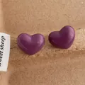 Detailed macro view of purple heart-shaped stud earrings on a textured paper background - Heart / Purple