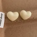Detailansicht der 3D herzförmigen Ohrstecker in Cremeweiß aus Harz auf Texturhintergrund - Herz / Gebrochenes Weiß