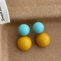 Dettaglio di orecchini a sfera blu e gialli lucidi su uno sfondo di carta ruvida - Blu/Giallo