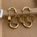 Nahaufnahme goldener C-förmiger Röhrenohrringe mit Kettenquasten auf einem Tablett - Gold (G26)
