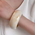 Detail of wide resin bangle with amber marble patterns on smooth cream surface - Off White