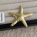 Dettaglio macro di spilla a stella marina dorata con trama ondulata su vassoio - Oro (P74)
