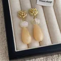 Close-up of teardrop earrings with golden rose studs and peach resin droplets - Off White