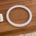 Nahaufnahme eines transluzenten weißen Armreifs auf dunklem Holztablett im minimalistischen Design - Weiß