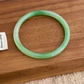 Macro detail of a smooth emerald green jade-style bangle on a natural wooden surface - Green