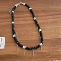 Detail van kralenketting met zwarte en witte kralen en hangende zilveren metalen kwastjes - Zwarte Kwastje / Zwart