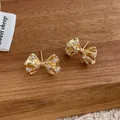 Detailed close-up of golden bow-shaped stud earrings with zircon crystals on wood - Bowknot Shape (Gold)