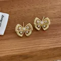 Détail macro de boucles d'oreilles papillon dorées avec zircons sur bois sombre - Boucles d'oreilles Papillon / Or