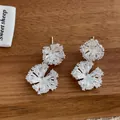 Makroaufnahme der silbernen Blumenohrringe mit Zirkonia-Pavé auf Holzhintergrund - Doppelrunde Zirkonia Ohrringe (Silber)