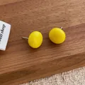 Close-up of vibrant yellow button stud earrings on wood and cream fabric background - Yellow