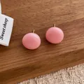 Detail view of pink round stud earrings with smooth finish on a wooden display - Pink