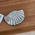 Vue rapprochée d'une broche coquillage argentée avec texture métallique rainurée - Style Coquillage / Argenté