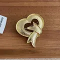 Detail einer goldenen Herzbrosche mit Hammerschlag-Textur und Schleifendesign auf Holz - Gold