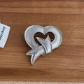 Detail der silbernen Herzbrosche mit Schleifen-Design und Hammerschlag auf Holzgrund - Silber