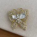 Macro shot of gold butterfly brooch with zircon crystals on warm beige fabric - Gold