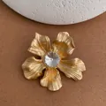 Vintage gold matte flower brooch with a large crystal center on a textured background - Gold