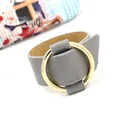 Wide gray leather cuff bracelet featuring a large polished gold metal ring accessory - Gray