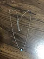 Detail of silver chain with Evil Eye pendant featuring lobster clasp on wooden background - Green Eye Steel