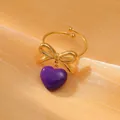 Detail of golden bow ring featuring a purple enamel heart charm on silk fabric - Purple Character