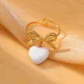 Detailed view of golden bow ring with white heart pendant on elegant silk fabric - White Style
