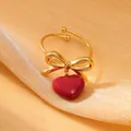 Close-up of golden bow ring with dark red heart pendant on gold silk background - Deep Red Style