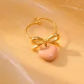 Detailed close-up of a gold-plated bow ring with a hanging pink heart-shaped pendant - Soft Pink Style