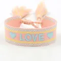 Close-up of pink woven LOVE friendship bracelet with colorful embroidery and fringe tassels - L004 LOVE / Macaron Color